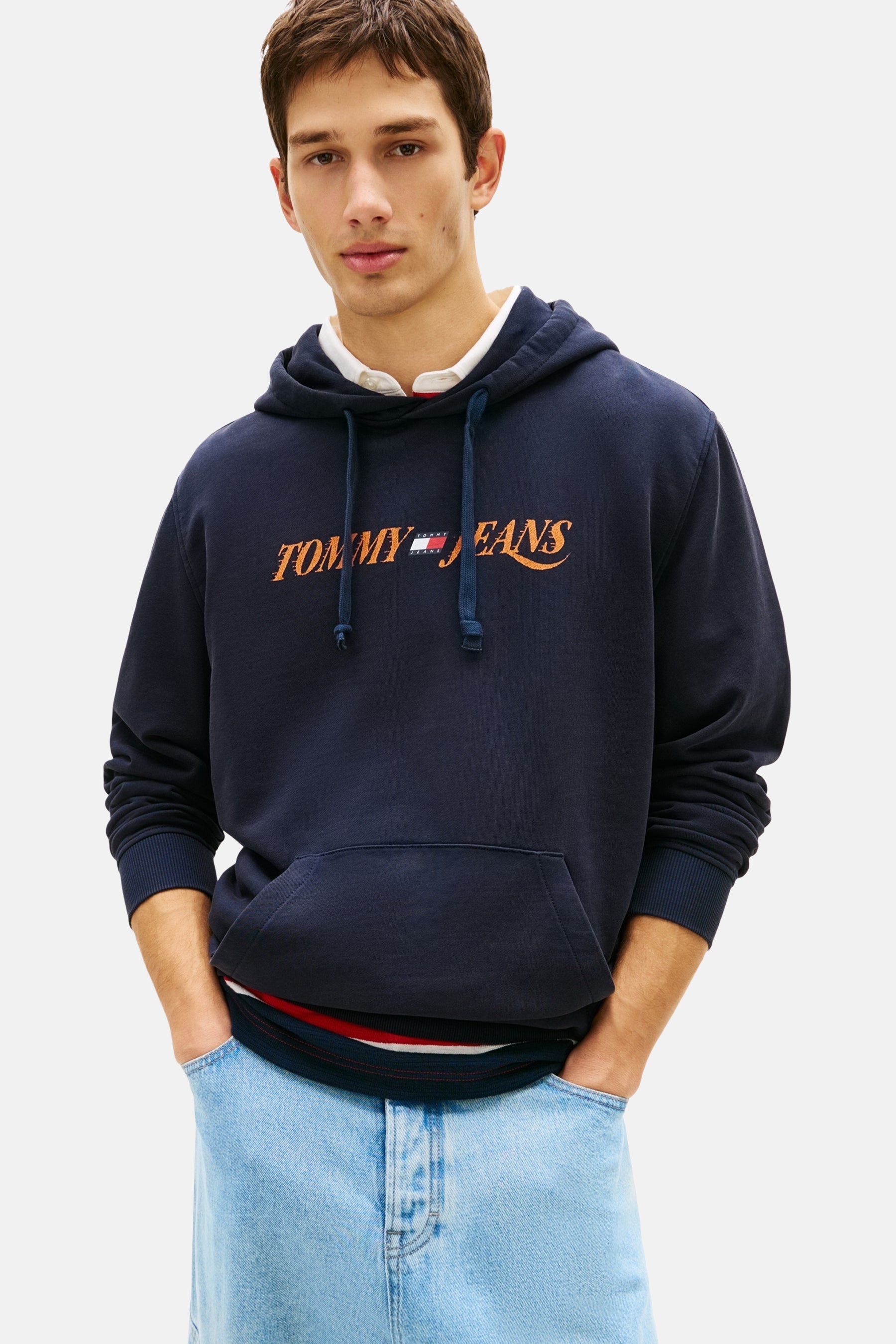 Sweat à capuche bleu marine de TOMMY JEANS avec cordon de serrage et logo orange, porté avec un jean bleu clair.