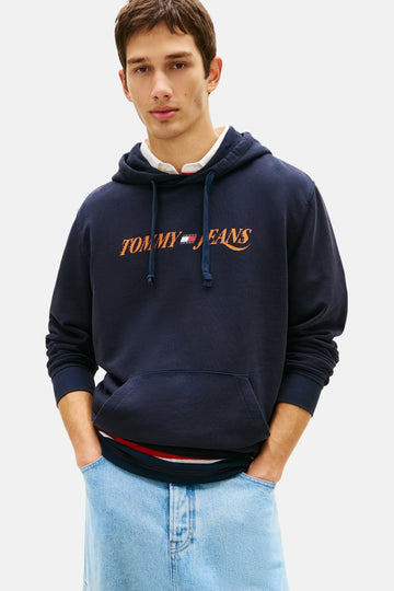 Sweat à capuche bleu marine de TOMMY JEANS avec cordon de serrage et logo orange, porté avec un jean bleu clair.